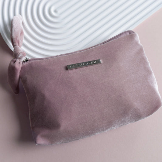 A pink velvet clutch with a silver pin that says DERMATUDE.